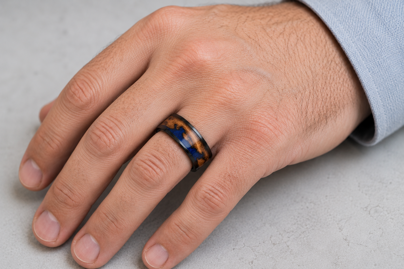 A close-up of a person's hand wearing a dark ring with a marbled pattern of black, brown, and blue.