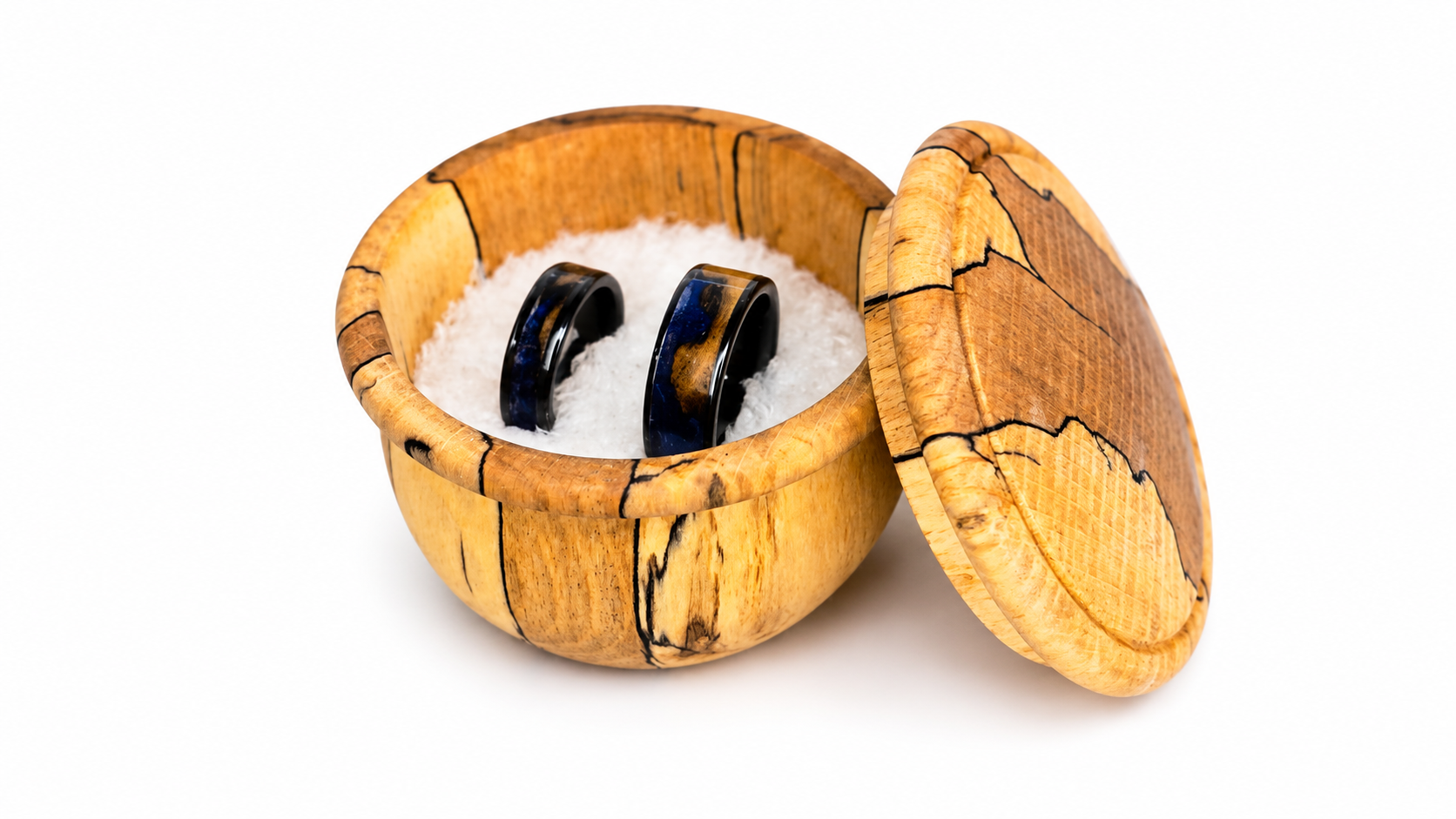 Two dark metallic rings displayed inside a small carved wooden box with the lid propped beside it on a white background.