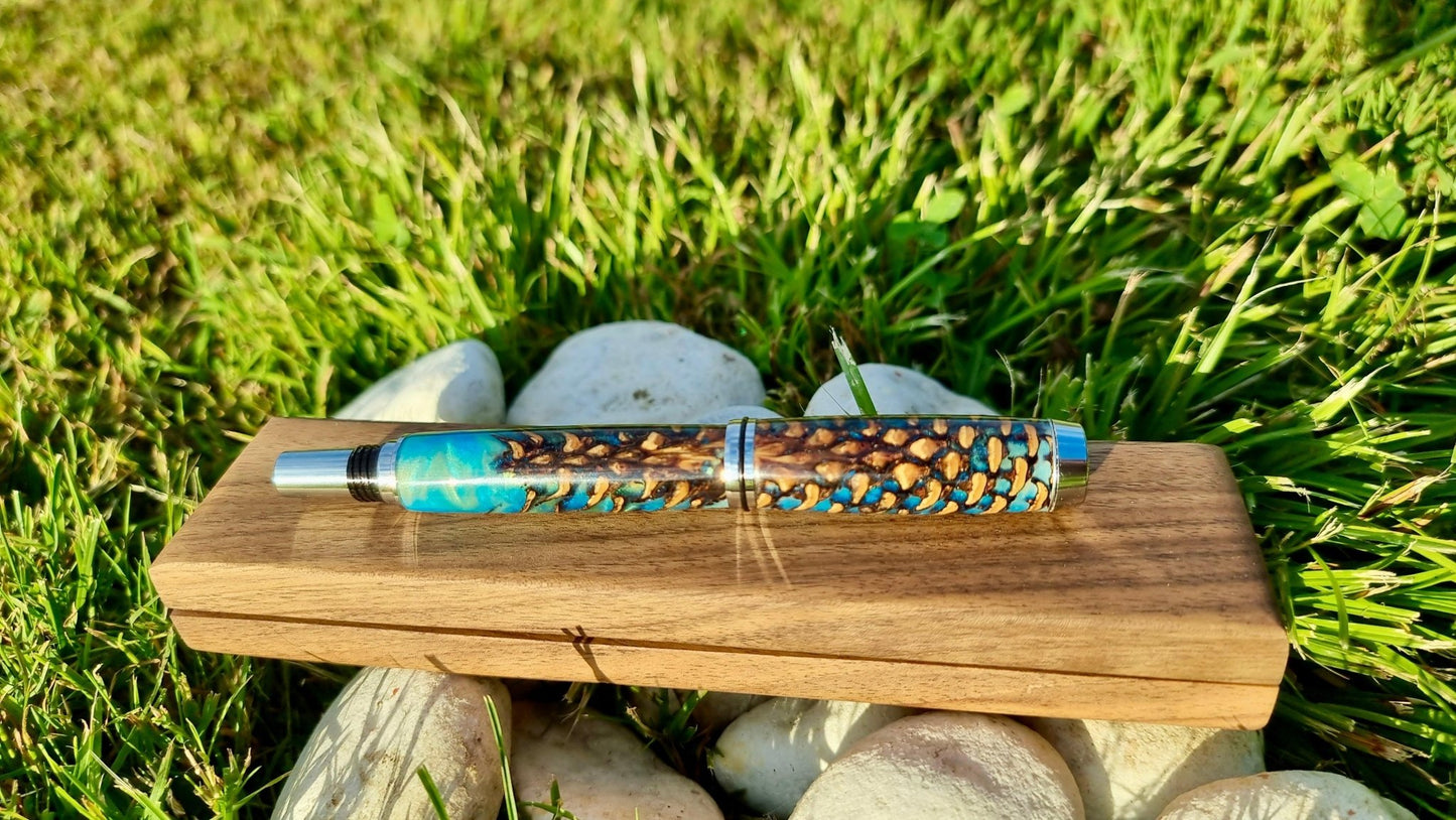 Artisan epoxy resin fountain pen with natural pine cones photographed on grass background